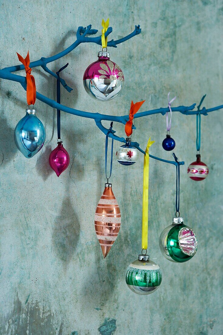 Multicoloured Christmas baubles hang against faded turquoise background