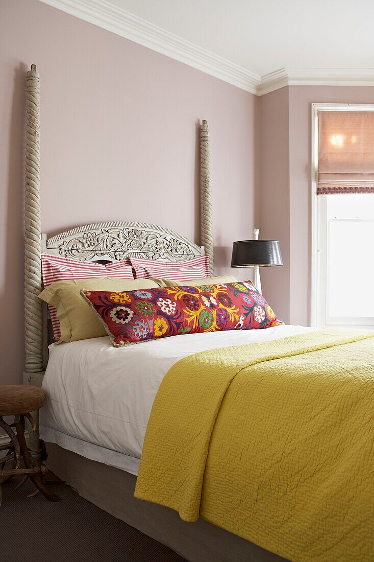 Blumenkissen auf geschnitztem antiken Bett mit gelber Decke in einem Londoner Haus UK