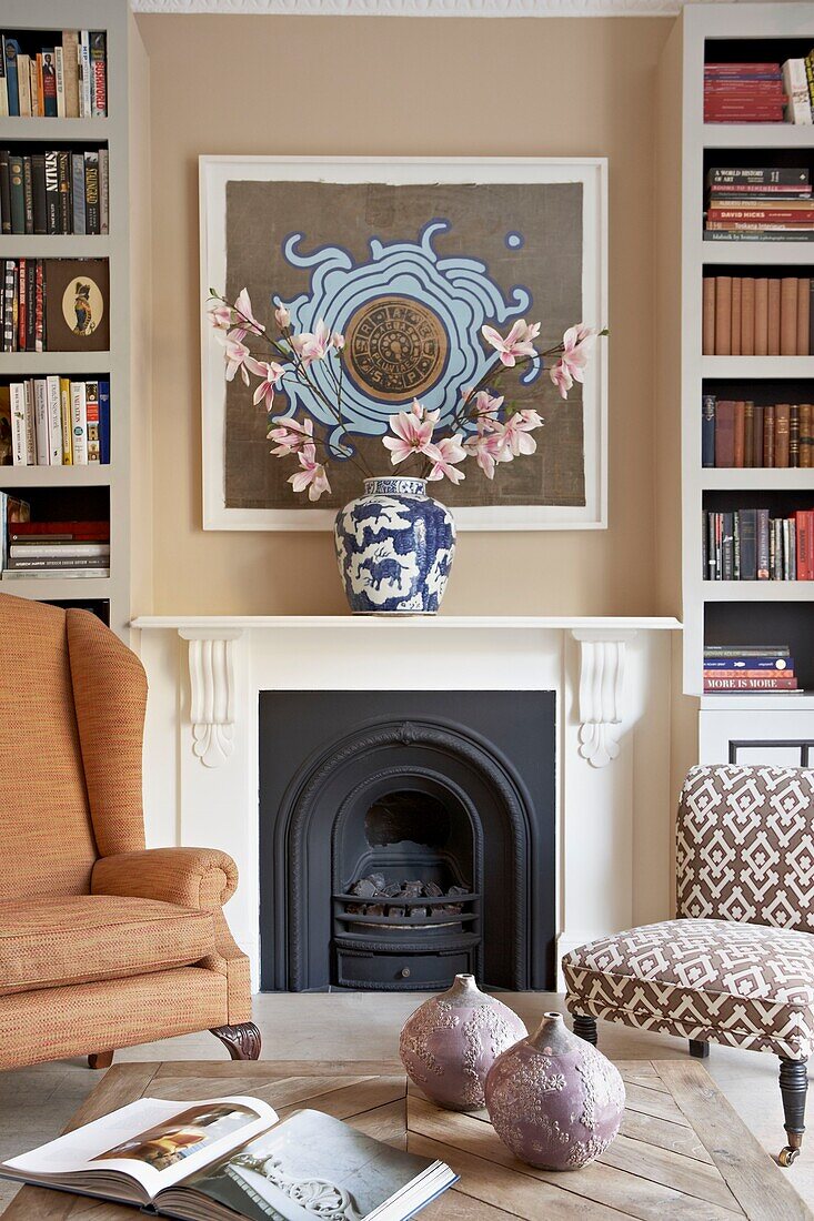 Lilien auf dem Kaminsims mit gepolsterten Stühlen und Bücherregalen im Wohnzimmer einer Londoner Wohnung UK
