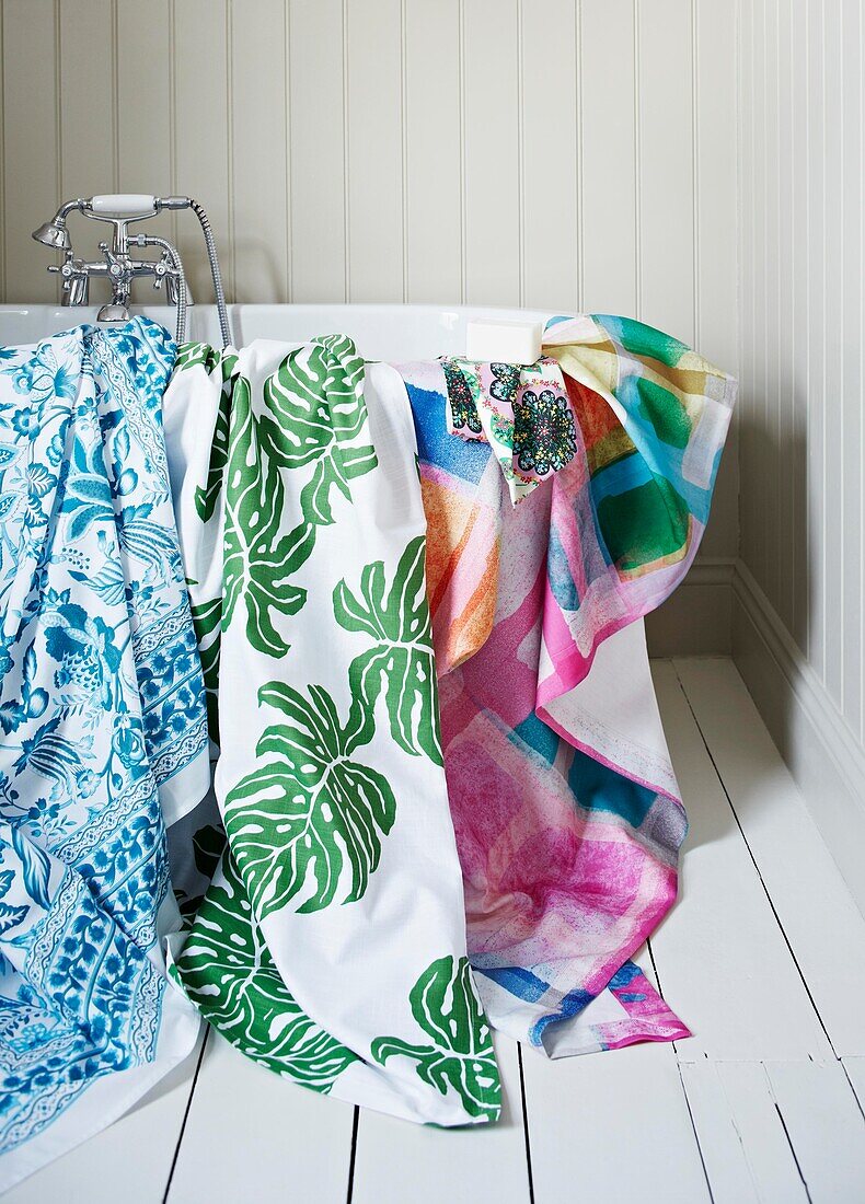 Multicoloured towels on bathtub in white panelled bathroom of family home