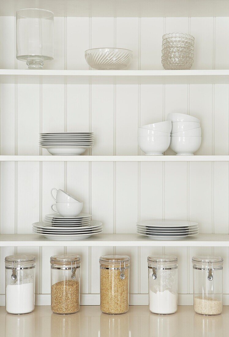 Bowls and plates with storage jars on panelled kitchen shelf detail