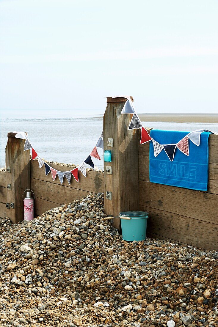 Beach scene with groin and bunting draped over it and barbecue and flask for picnic