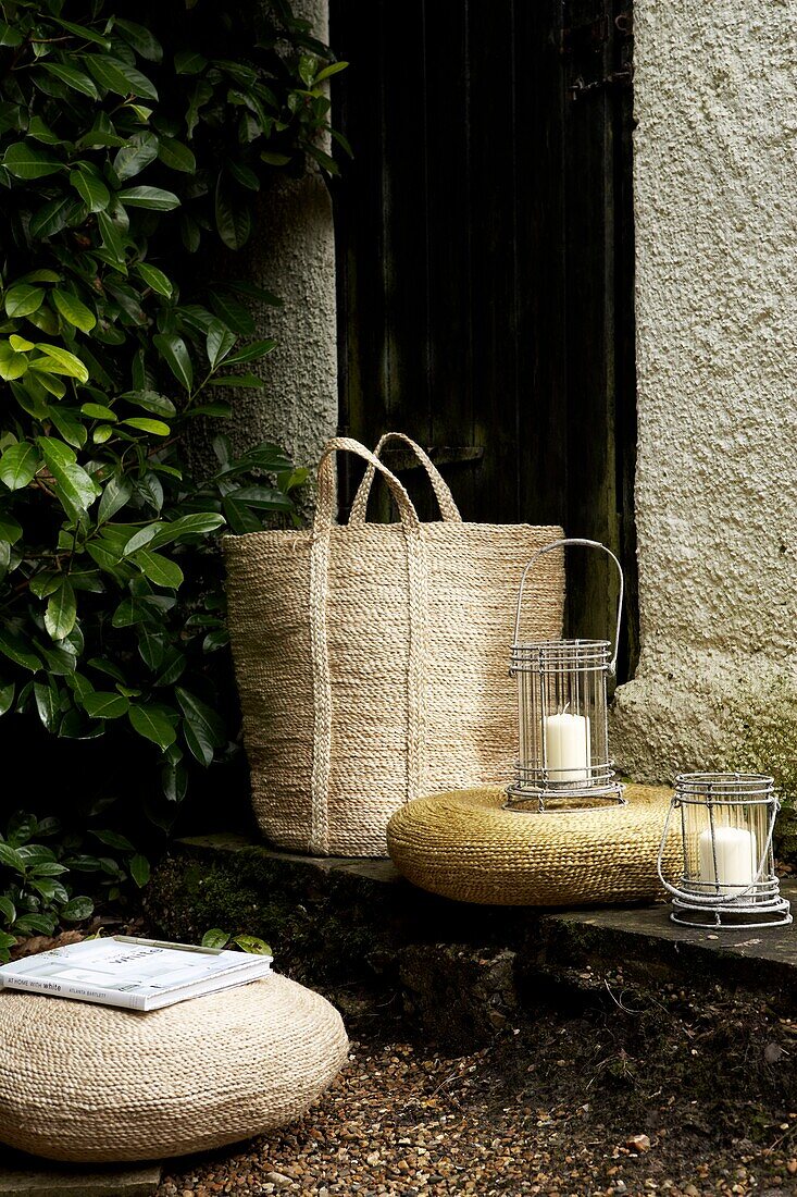 Rattan pouffes and large wicker basket with lanterns in corner of a garden