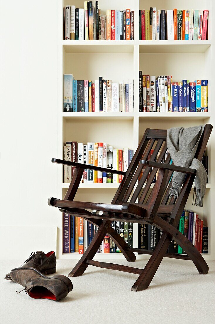 Sessel und Bücherregal aus dunklem Holz mit Schal und Herrenschuhen