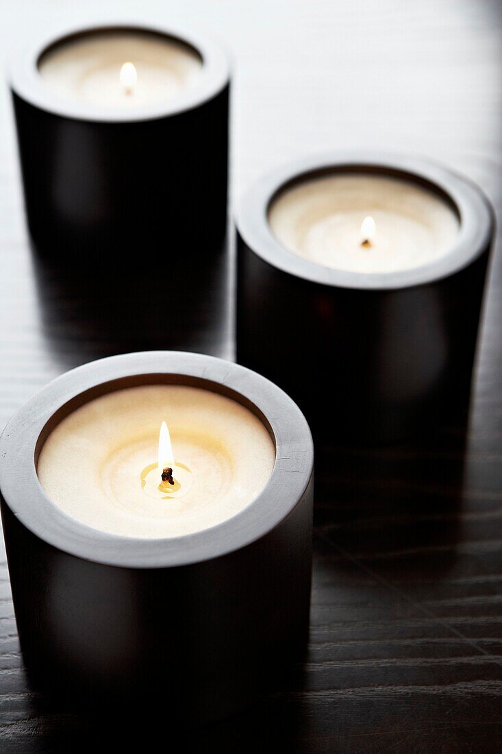Drei brennende Kerzen in Kerzenhaltern aus dunklem Holz