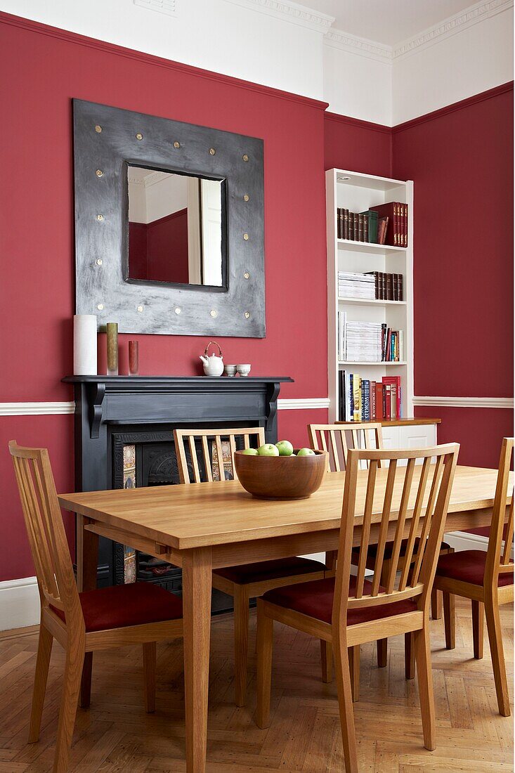 Square mirror above fireplace in red living room with wooden dining table and chairs