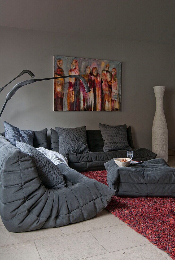 Graue Sitzgelegenheit mit Kunstwerk auf Leinwand im Wohnzimmer eines modernen Hauses in Haywards Heath, West Sussex, England, UK