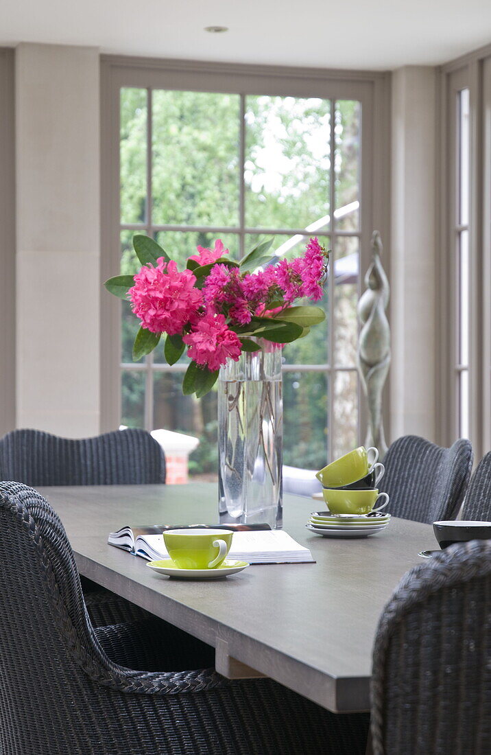 Pink flowers with lime green teacups on dining table in contemporary Haywards Heath home,  West Sussex,  England,  UK