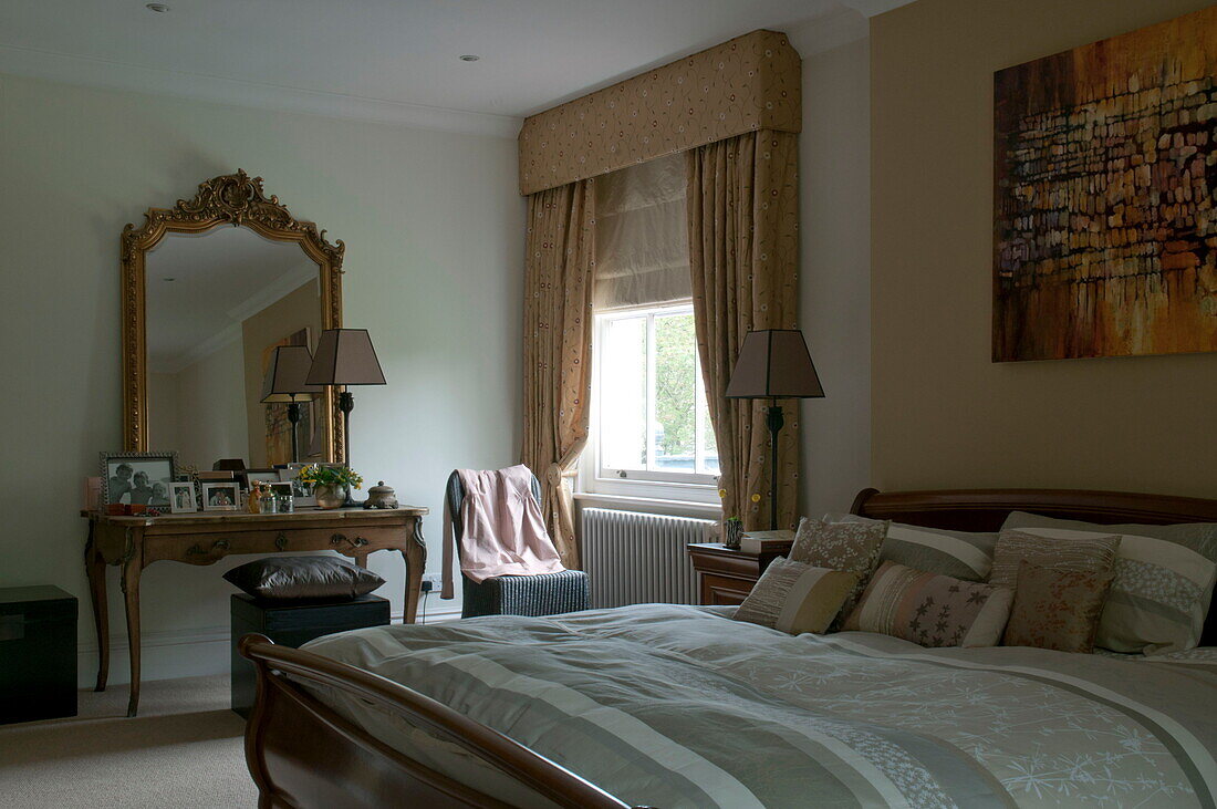 Gilt framed mirror on dressing table of bedroom with gold curtains and striped duvet in Haywards Heath home,  West Sussex,  England,  UK