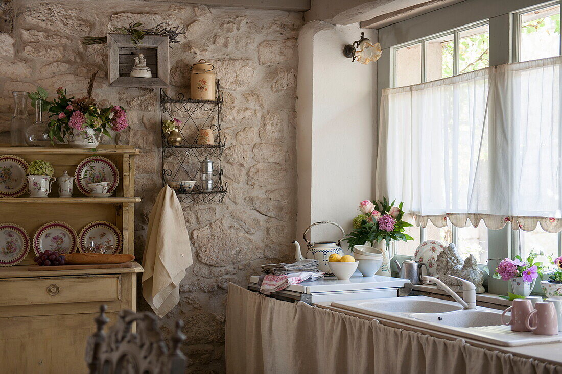 Net curtains above sink in kitchen of stone farmhouse,  Dordogne,  France
