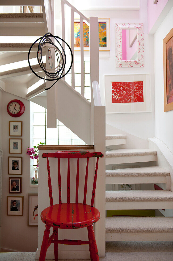 Red painted chair with artwork in staircase of Lewes home,  East Sussex,  England,  UK