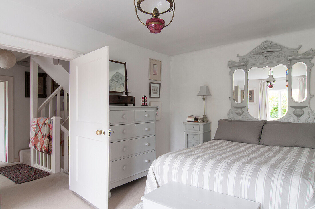 Geretteter Spiegel über gestreifter Bettdecke mit bemalter Kommode und Blick auf den Flur in einem Haus in Dorset, Kent, Großbritannien