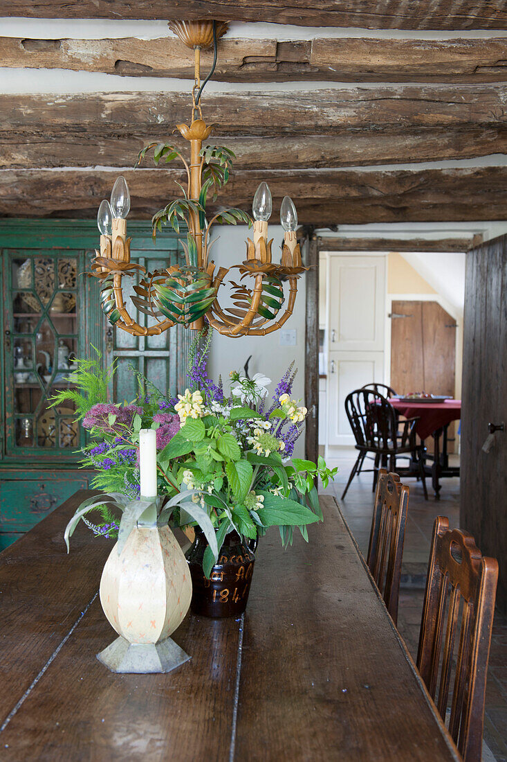 Cut flowers and chandelier with dining table and low beamed ceiling in Ashford farmhouse  Kent  UK
