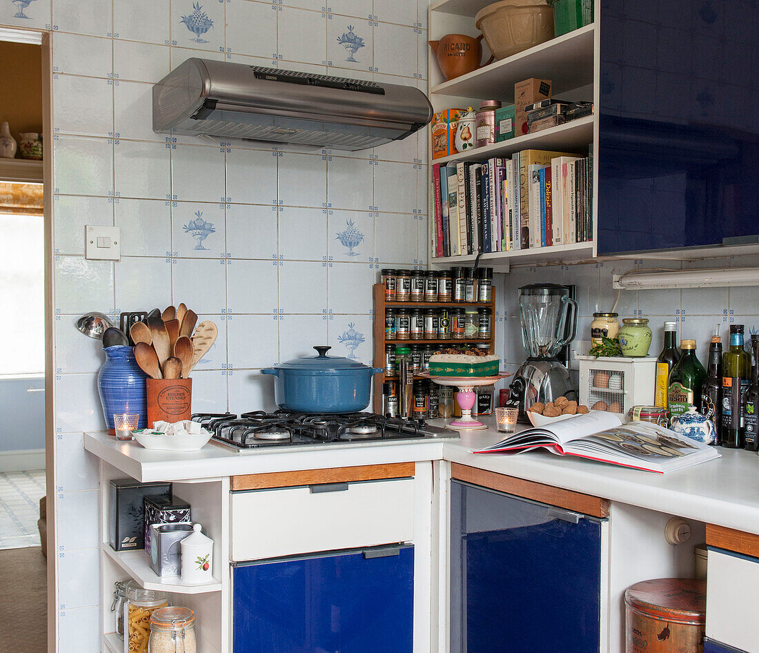 Holzlöffel und Gewürzregal mit Kasserolle auf dem Kochfeld in blauer Einbauküche in London England UK