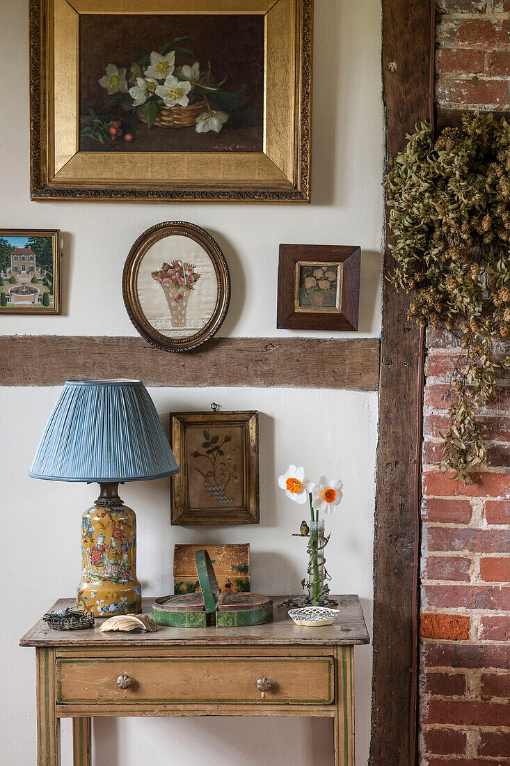 Framed vintage artwork above wooden side table in High Halden cottage  Kent  England  UK
