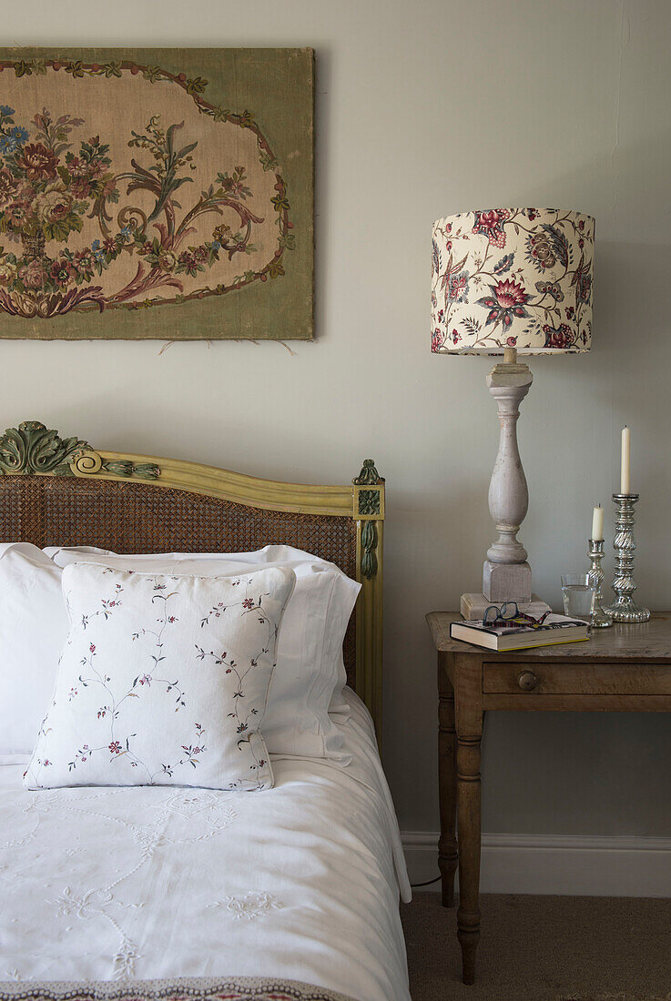 Wandteppich und florale Lampe mit silbernen Kerzenhaltern am Bett in East Barsham cottage Norfolk England UK