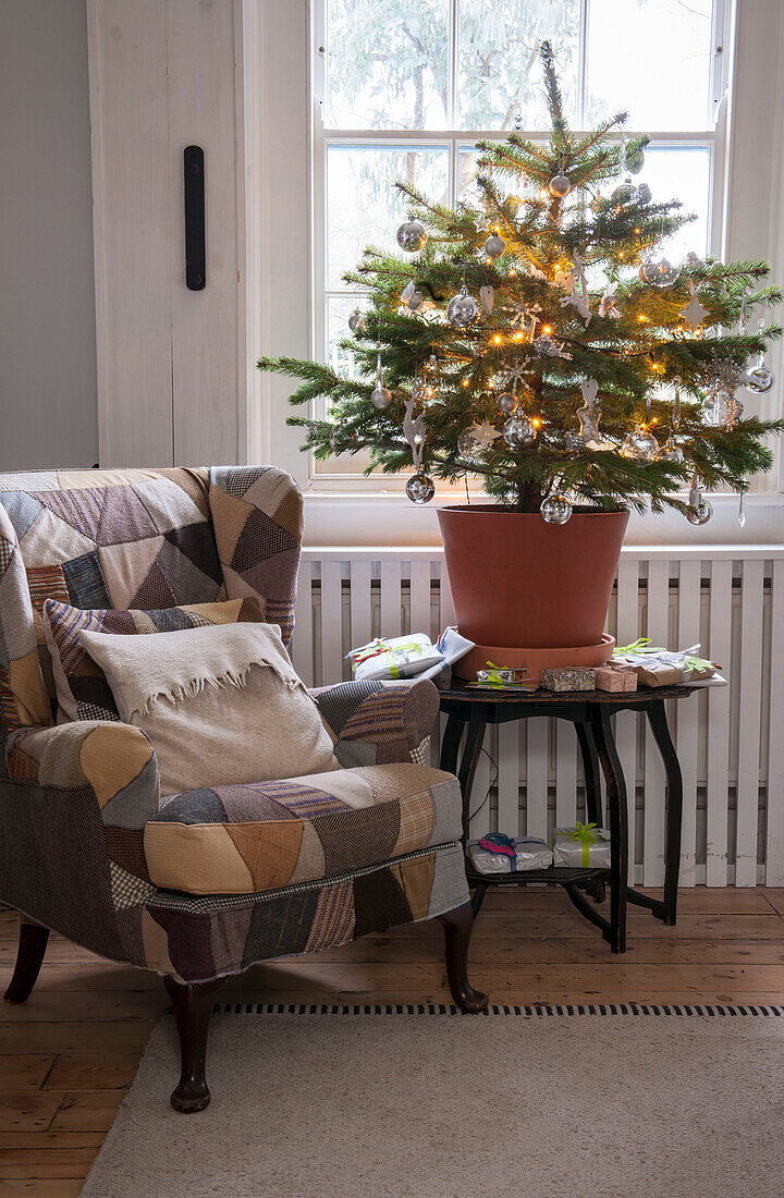 Patchwork-Sessel und Weihnachtsbaum mit beleuchteten Lichtern am Fenster in einem Londoner Haus in England UK