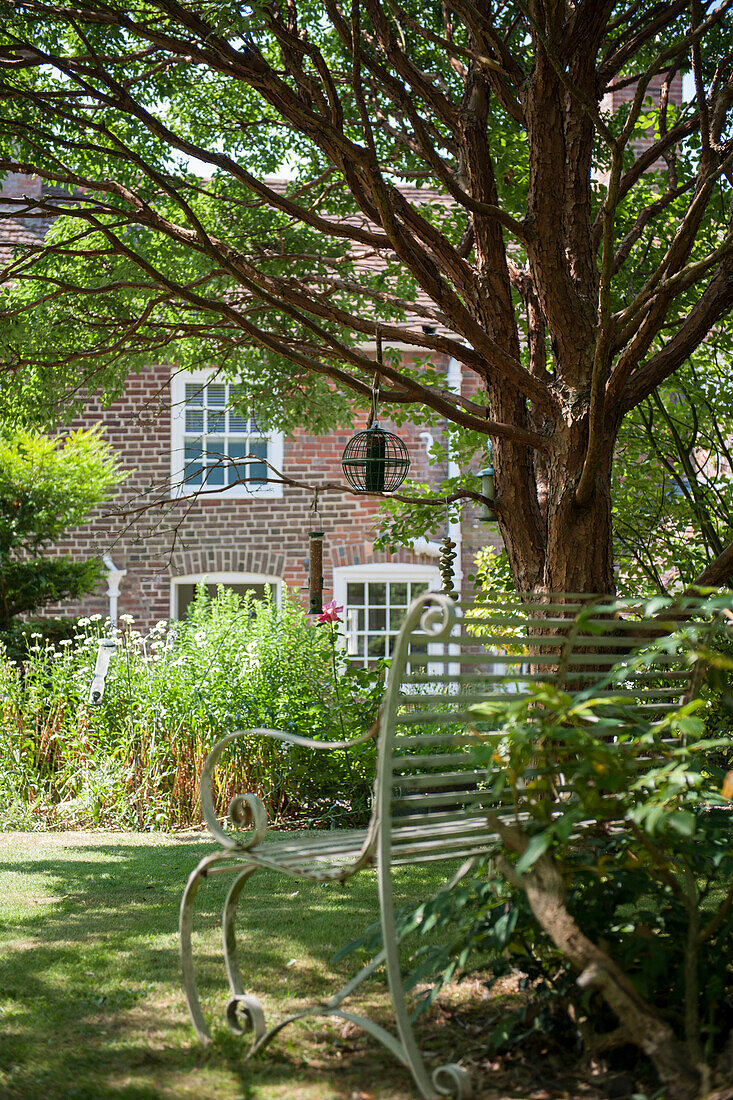 Bird feeder and metal bench under tree in garden of Kent home  England  UK