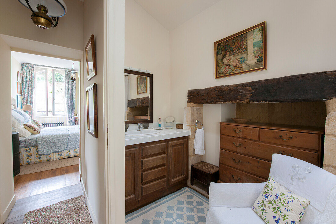 Waschbecken und Holztruhe mit Blick durch die Schlafzimmertür im Landhaus in der Dordogne, Frankreich