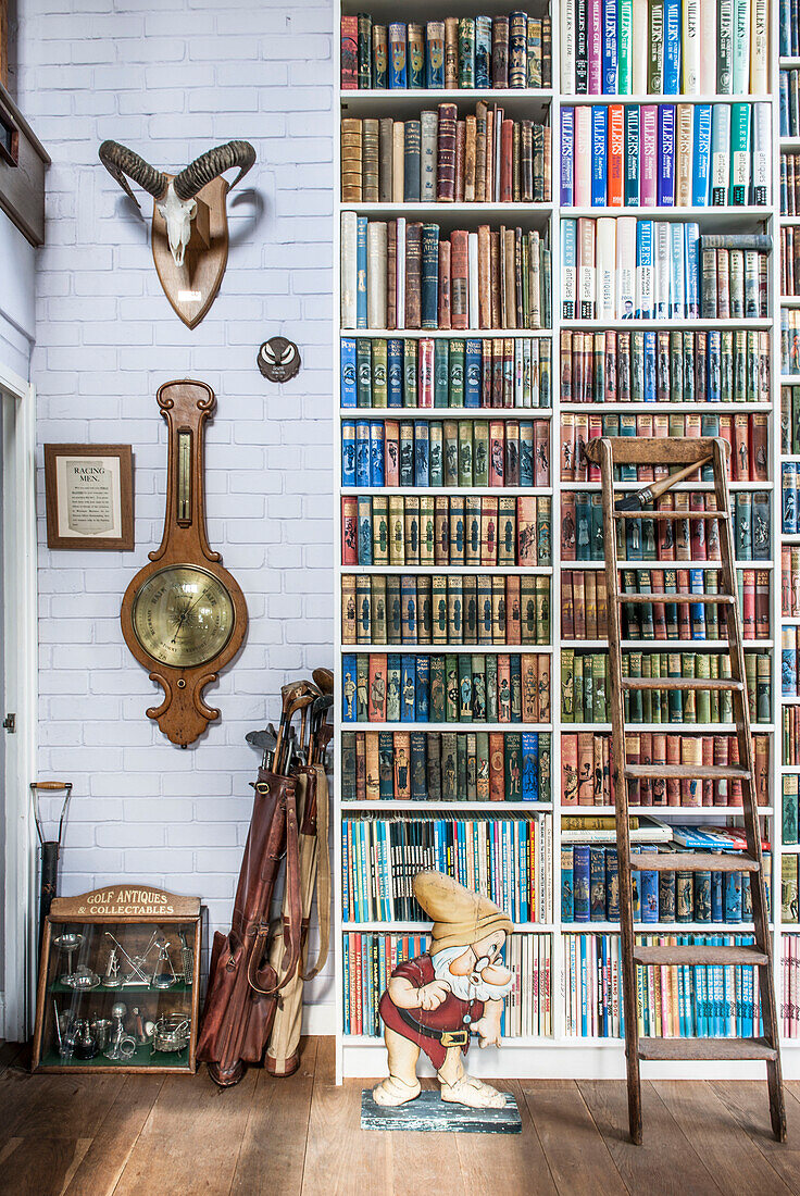 Barometer und goldene Keulen mit alten Büchern auf einem Regal in einem Cottage der Küstenwache in Norfolk, England, UK