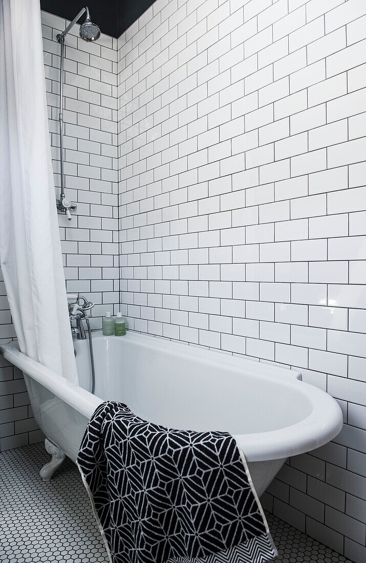 Freistehende Badewanne in einem weiß gefliesten Raum mit geometrischem Badvorleger in einem Haus in Whitstable, Kent England UK