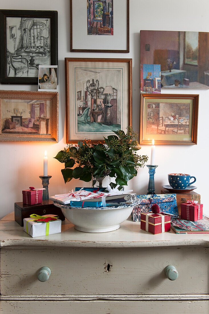 Gerahmtes Kunstwerk und brennende Kerzen mit eingepackten Geschenken in einem Haus in London, England, Vereinigtes Königreich