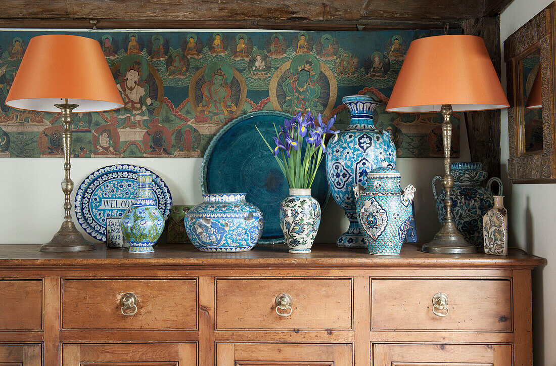 Pair of orange lamps with assorted blue chinaware and religious wall art in Suffolk home  England  UK