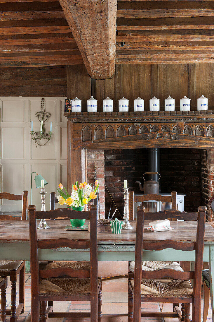 Dining chairs at table with carved fireplace under beamed ceiling in Suffolk home  England  UK