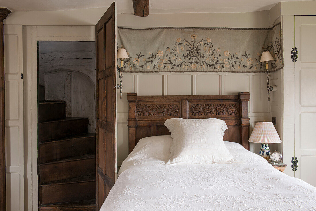 Embroidered fabric above carved antique bed in Suffolk home  England  UK