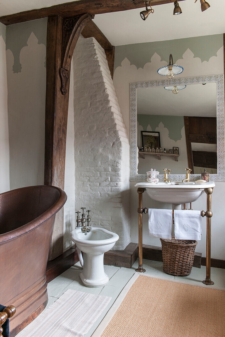 Waschbecken und Bidet mit Pantoffelbadewanne und freigelegtem, gekalktem Mauerwerk in einem Haus in Suffolk, England, UK