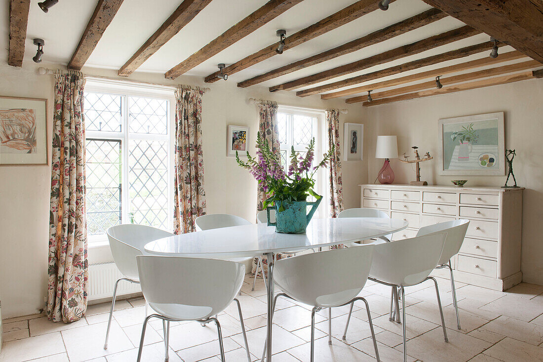 Schnittblumen auf modernem Esstisch und Stühlen unter Balkendecke in Suffolk-Bauernhaus England UK