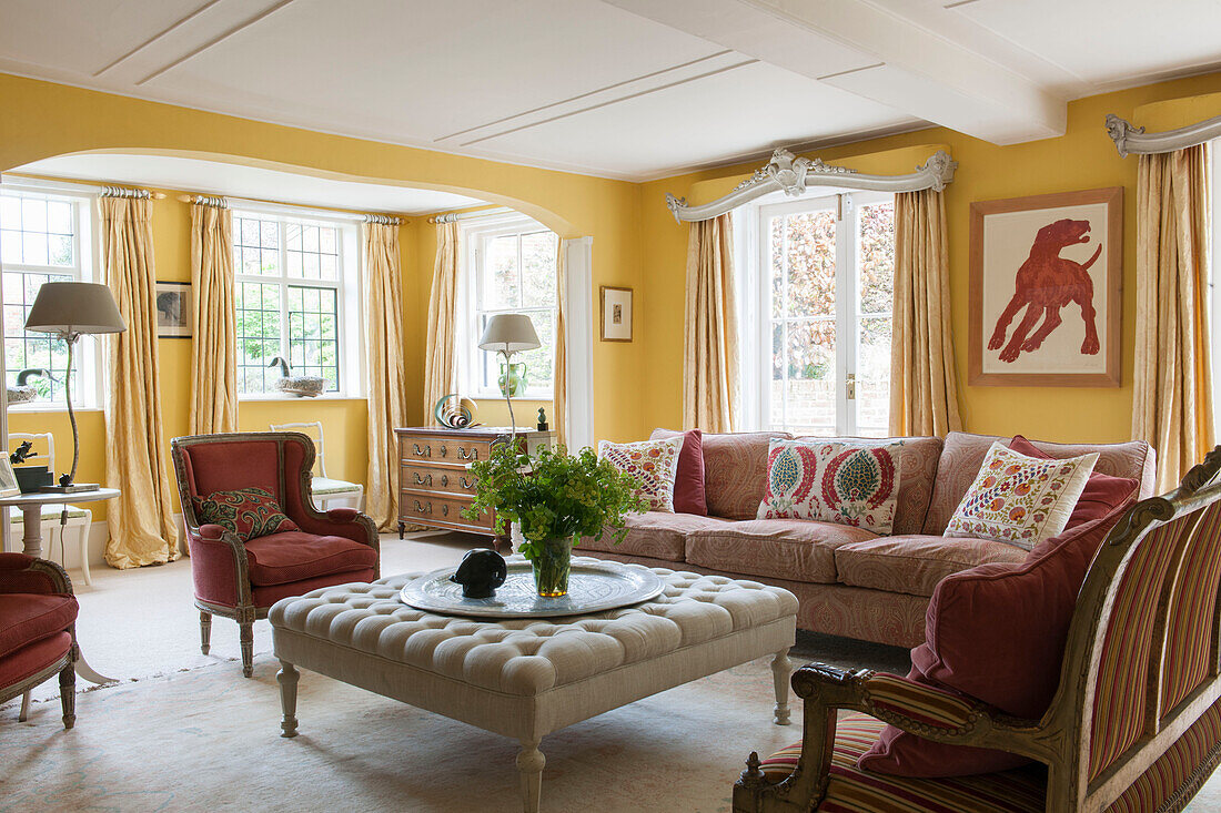 Red armchairs and sofa with large buttoned ottoman in yellow Suffolk living room  England  UK