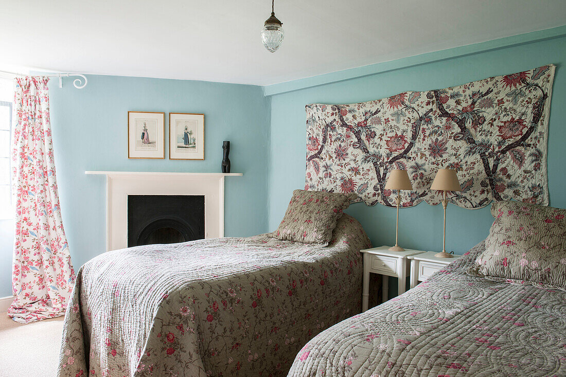 Zwillingsbetten mit geblümten Bezügen und Wandbehang in hellblauem Suffolk-Bauernhaus England UK