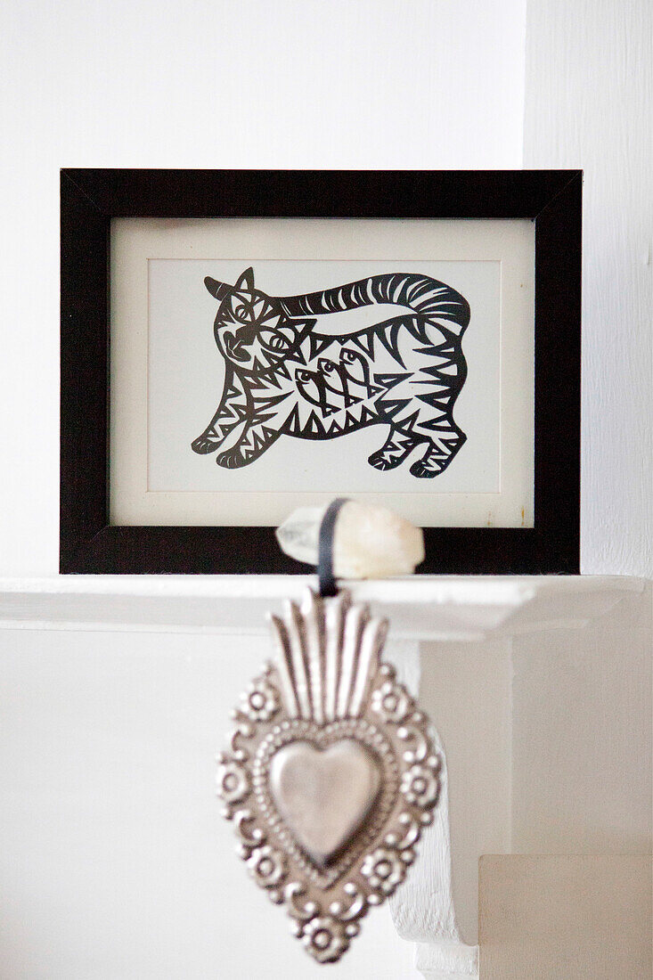 Gerahmtes Kunstwerk einer Katze und silbernes herzförmiges Ornament auf dem Kaminsims in Brighton, East Sussex England UK