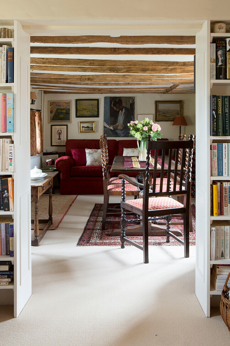 Blick auf Esstisch und rotes Sofa zwischen Bücherregalen in Amberley Cottage, West Sussex, UK