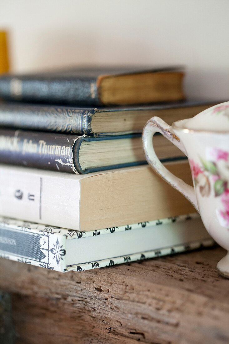 Gebundene Bücher und Porzellan auf einem Holzregal in Amberley cottage, West Sussex UK
