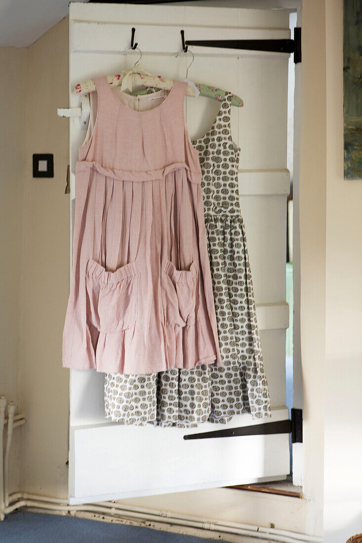 Pink and patterned dresses hang on back of door in Amberley cottage West Sussex UK