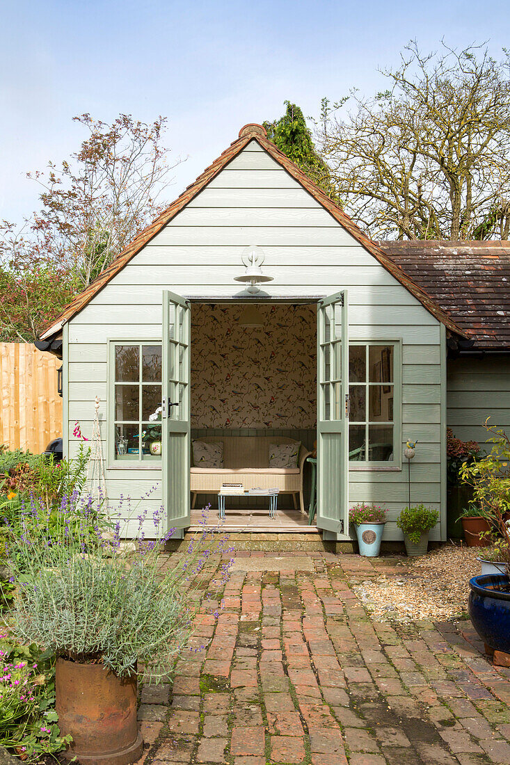 Hellgrünes Gartenhaus und gemauerter Weg im Garten eines Hauses in Amberley, West Sussex, Großbritannien