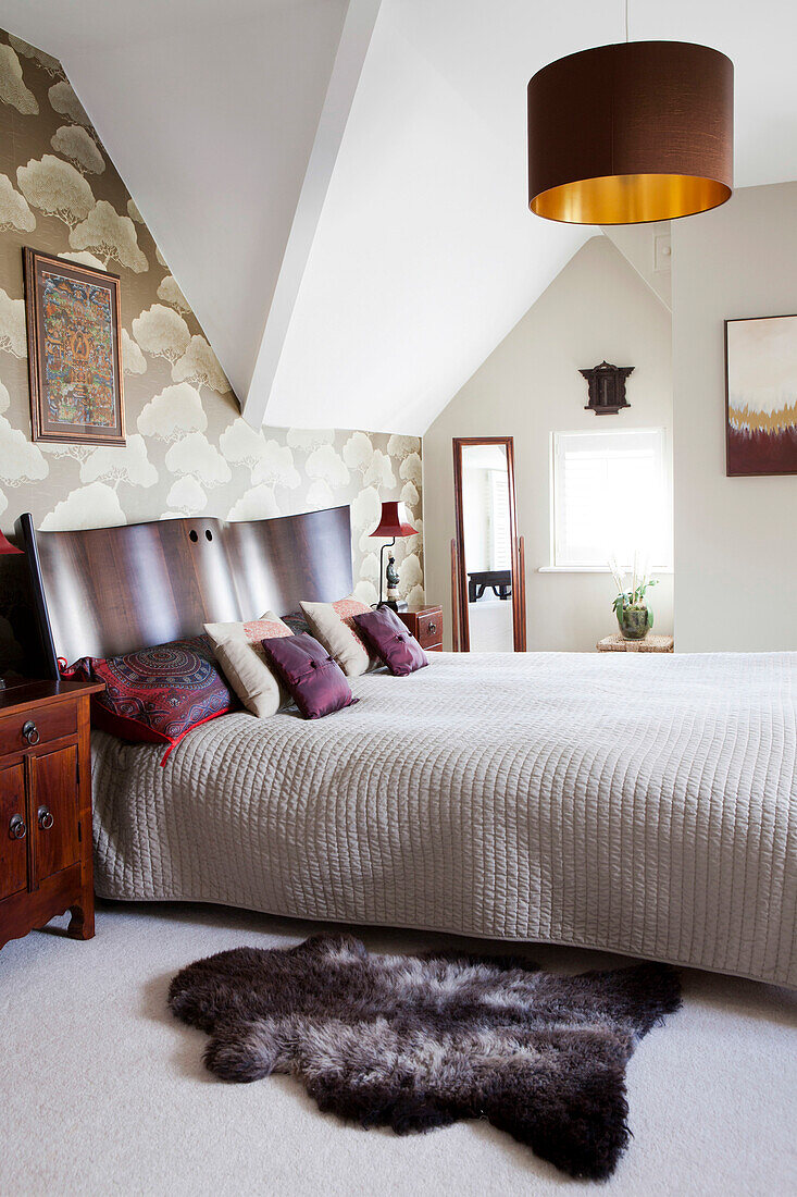 Pelzteppich am Bett mit geschwungenem Holzkopfteil im Haus in Amberley, West Sussex, England, UK