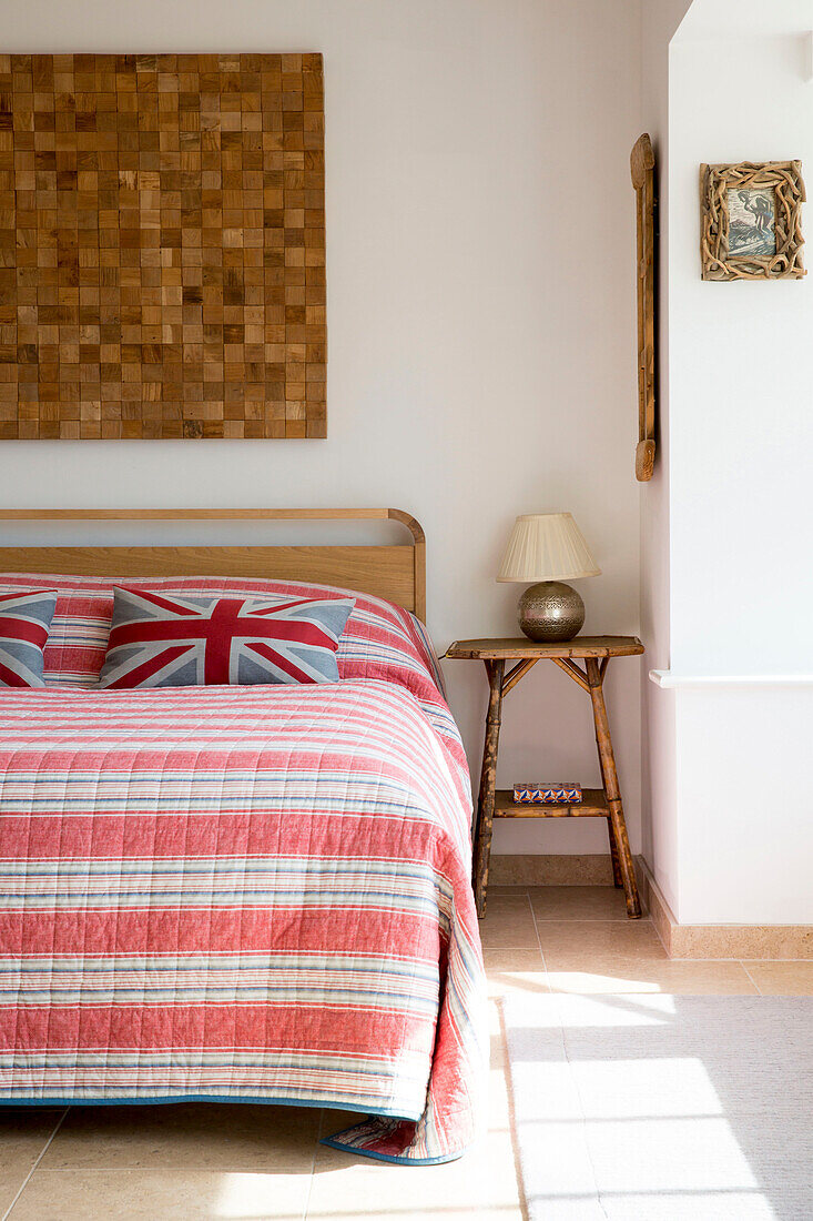 Gestreifter Bettbezug und Holzschnitt-Kunstwerk mit Beistelltisch in einem Haus in West Wittering, West Sussex, England
