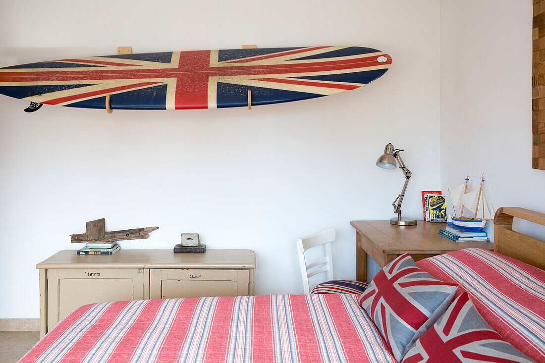 Union Jack Surfbrett mit Schreibtischlampe und gestreiften Bettbezügen in einem Haus in West Wittering, West Sussex, England
