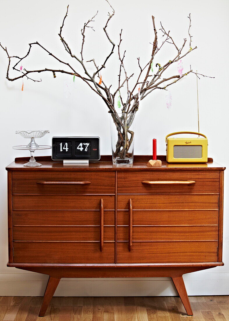 retro style wooden sideboard with twig arrangement and vintage clock and radio in London family home  England  UK