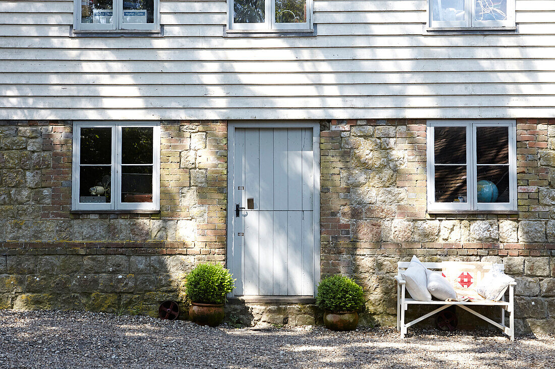 Sunlit bench with stone and weatherboard entrance to rural United Kingdom home