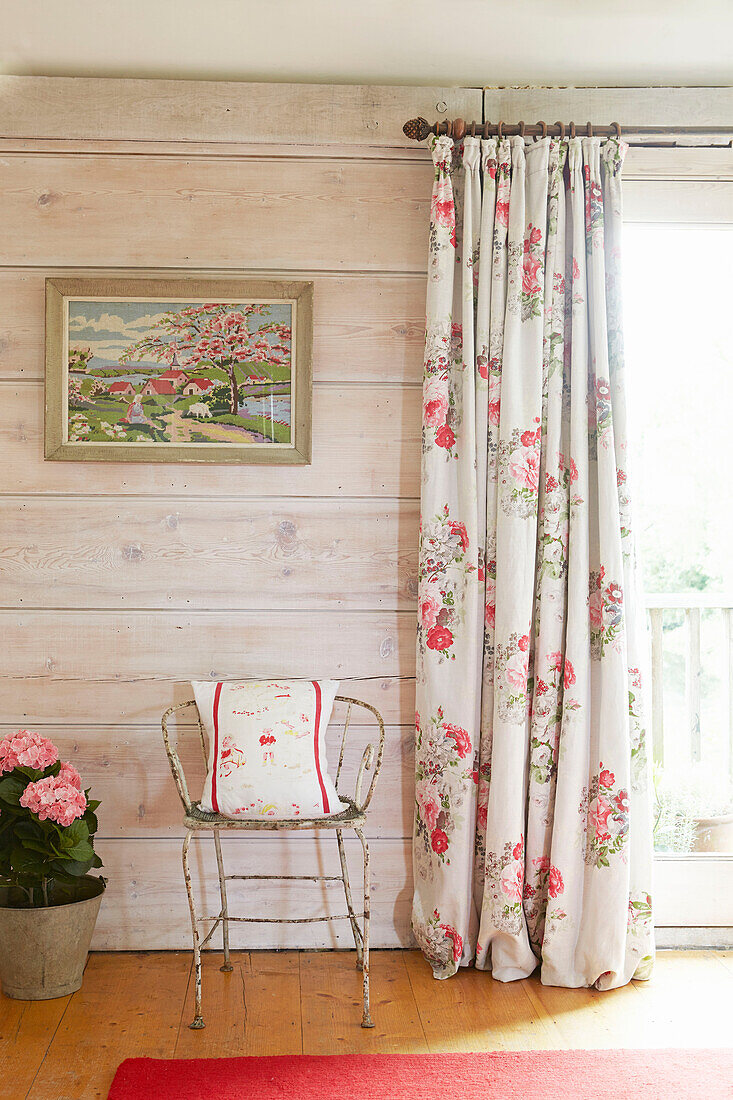 Alter Metallstuhl mit Kissen an der Terrassentür mit Kunstwerk in einem britischen Bauernhaus