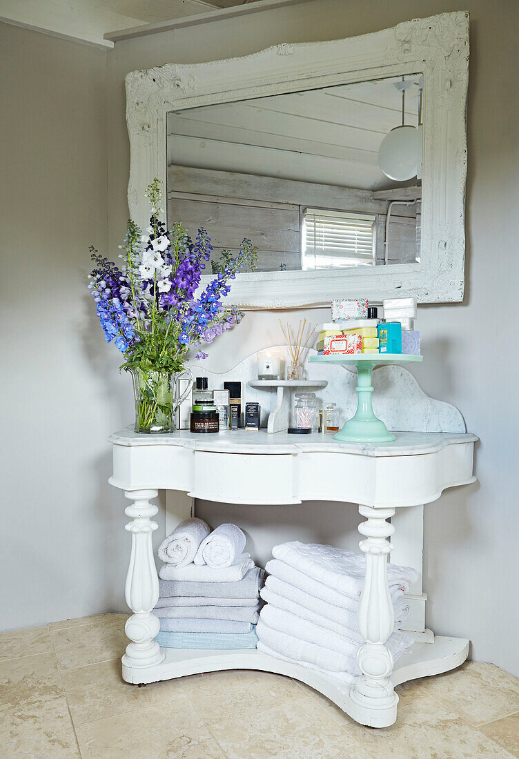 Toiletries and folded towels with cut flowers on wash stand in UK farmhouse