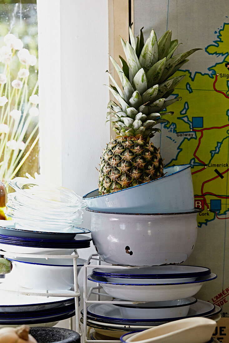 Pineapple on stacked metal bowls at sunlit kitchen window of Brabourne farmhouse,  Kent,  UK