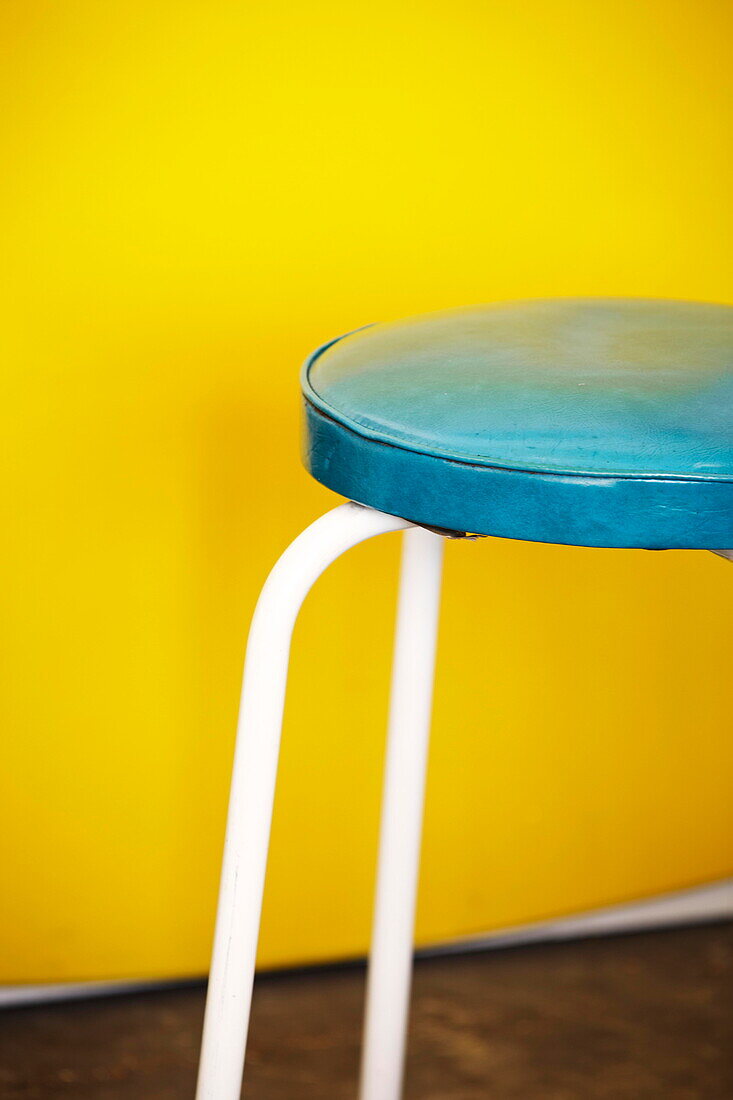 Turquoise leather stool set against yellow wall in Birmingham home  England  UK