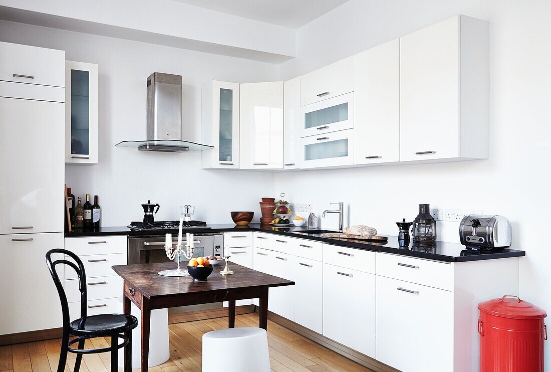 White fitted kitchen with wooden table and red dustbin in contemporary London family home   England   UK