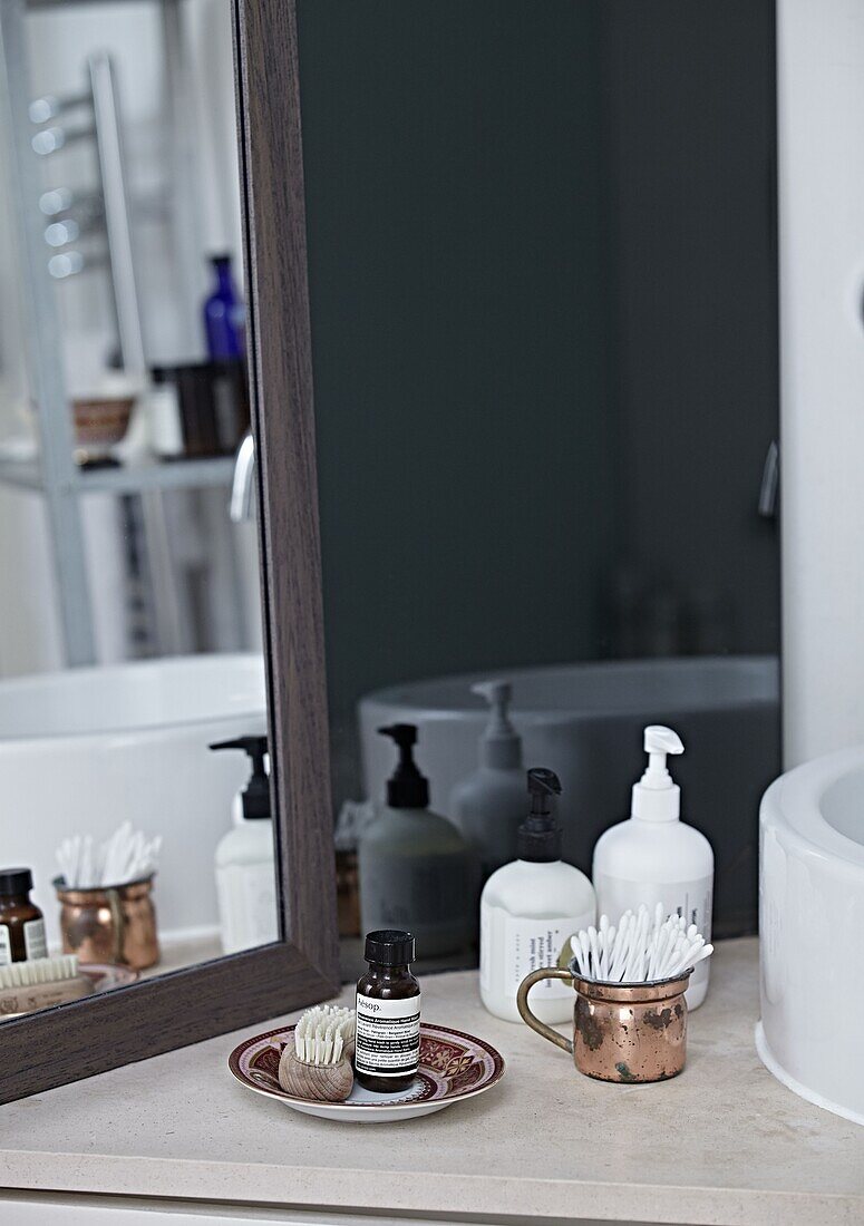 Soap dispensers and cotton buds with mirror in bathroom of contemporary London home   England   UK