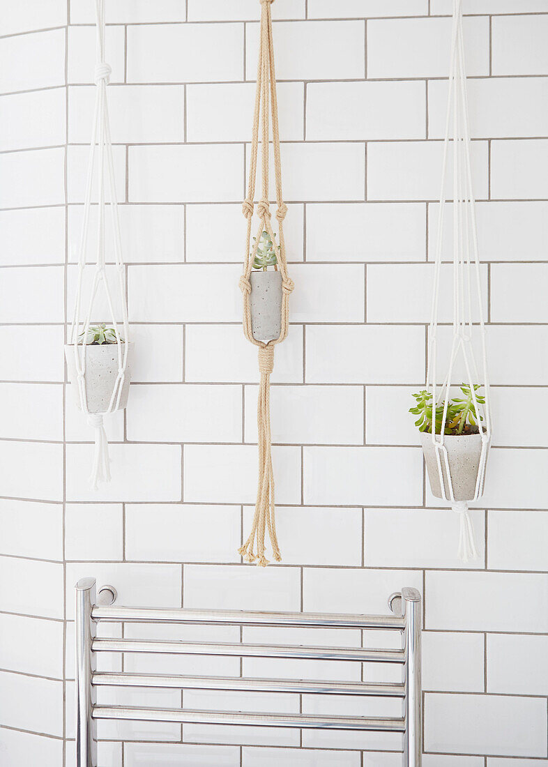 Rope plant hangers above wall-mounted radiator in white tiled London bathroom  UK